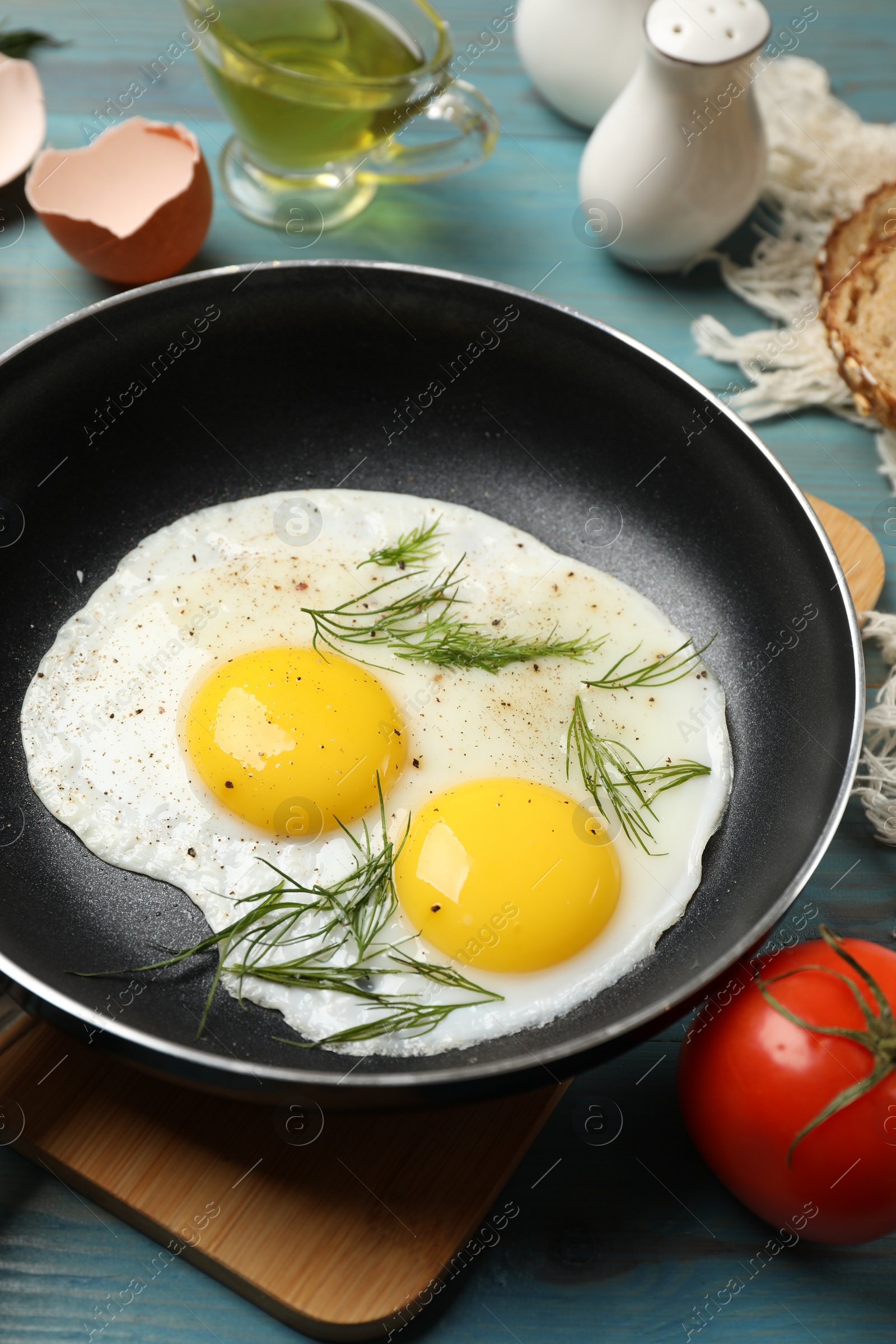 Photo of Frying pan with tasty cooked eggs, dill and other products on light blue wooden table, closeup