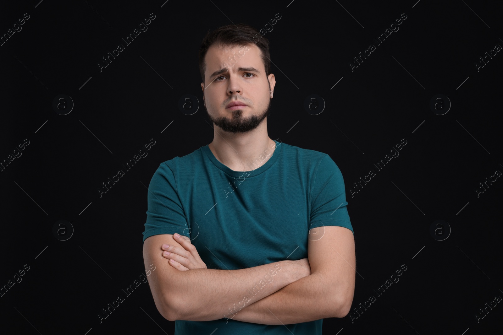 Photo of Portrait of sad man with crossed arms on black background