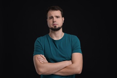 Portrait of sad man with crossed arms on black background