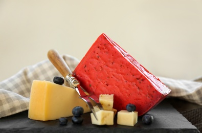Photo of Different delicious cheeses, fork and blueberries on slate plate, closeup