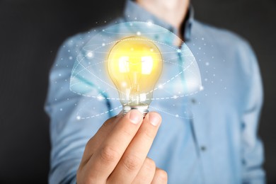 Image of Glow up your ideas. Man holding light bulb on dark background, closeup