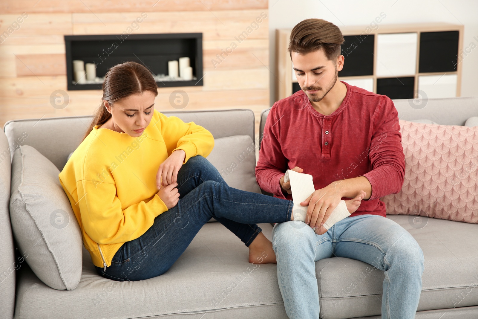 Photo of Young man applying bandage on woman's injured leg at home. First aid