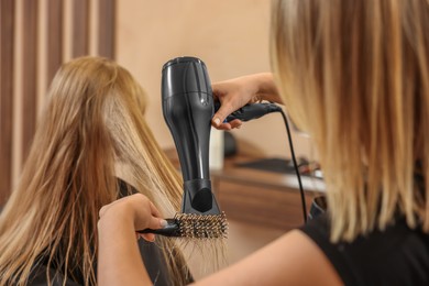 Photo of Professional hairdresser drying girl's hair in beauty salon, closeup