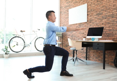 Photo of Young businessman doing exercises in office. Workplace fitness