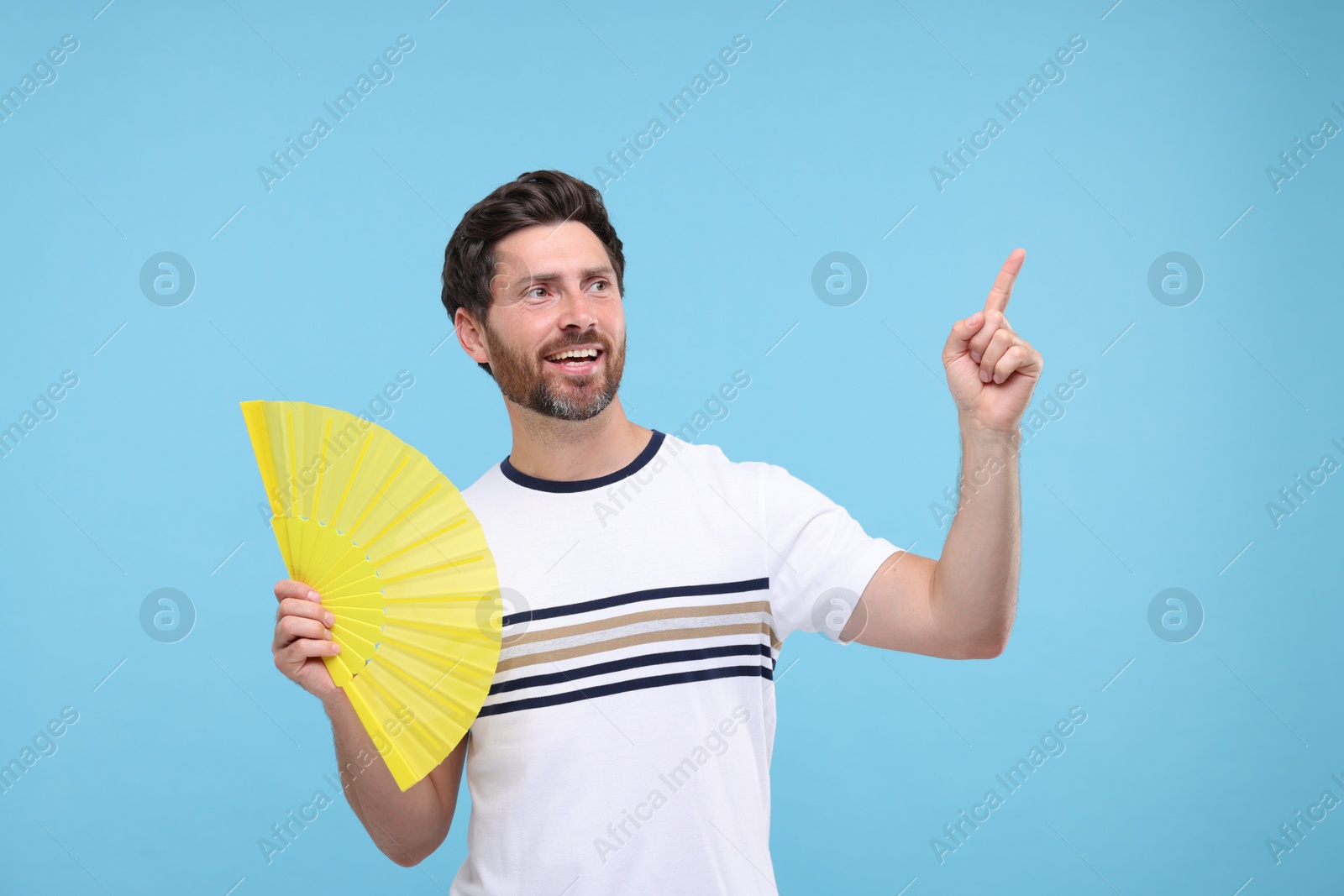 Photo of Happy man holding hand fan on light blue background