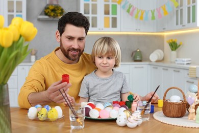 Father and his cute son painting Easter eggs at table in kitchen
