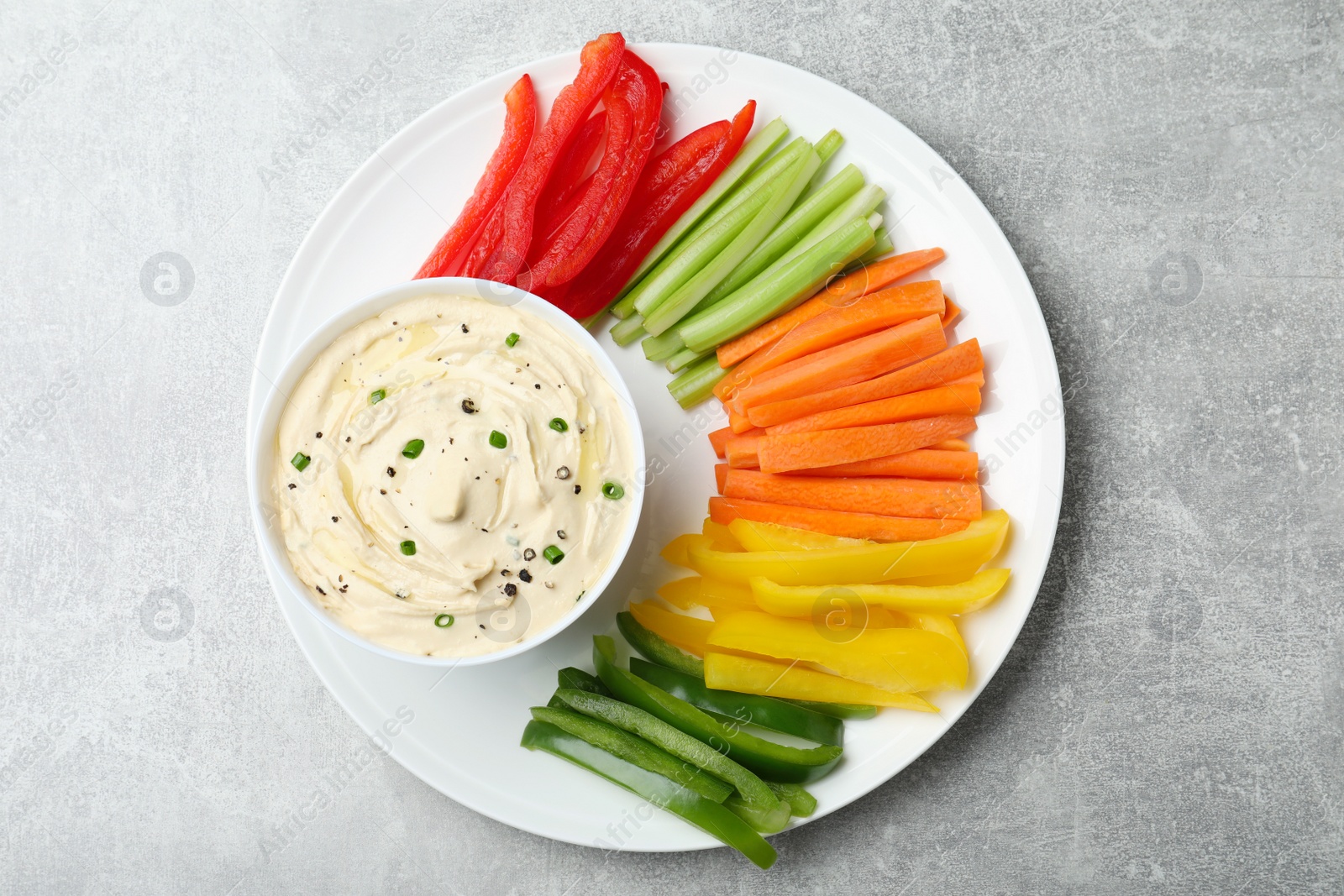 Photo of Fresh raw vegetable sticks and sauce on grey table, top view