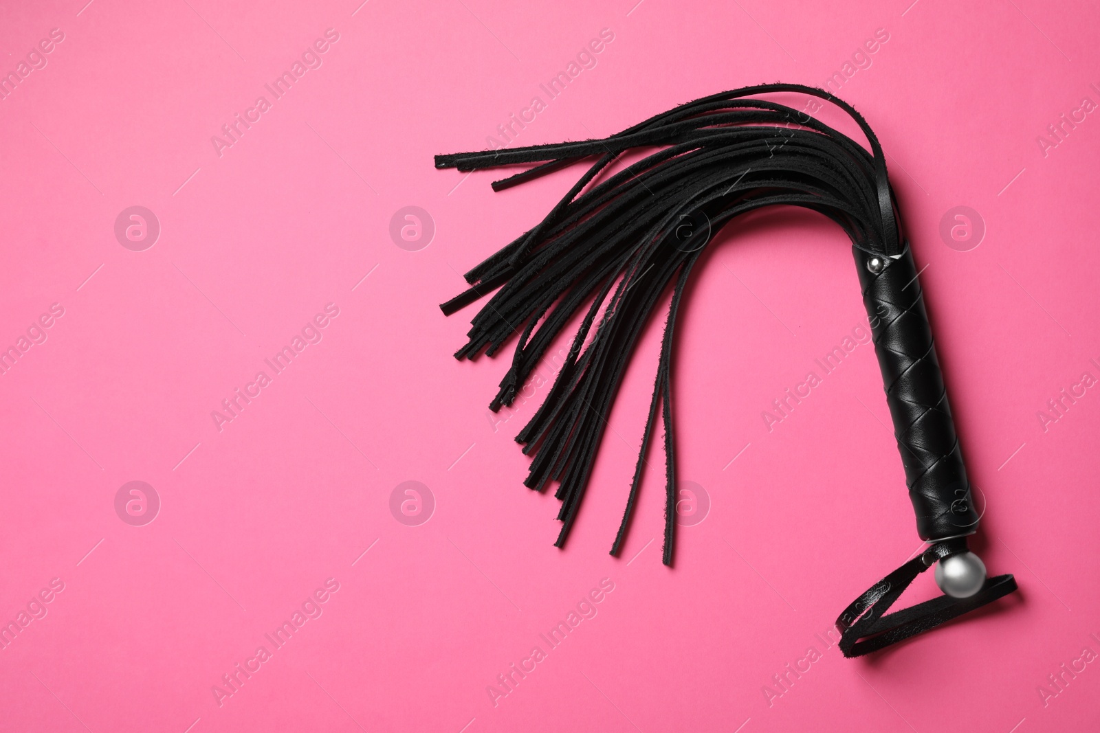 Photo of Black whip on pink background, top view with space for text. Sexual role play accessory