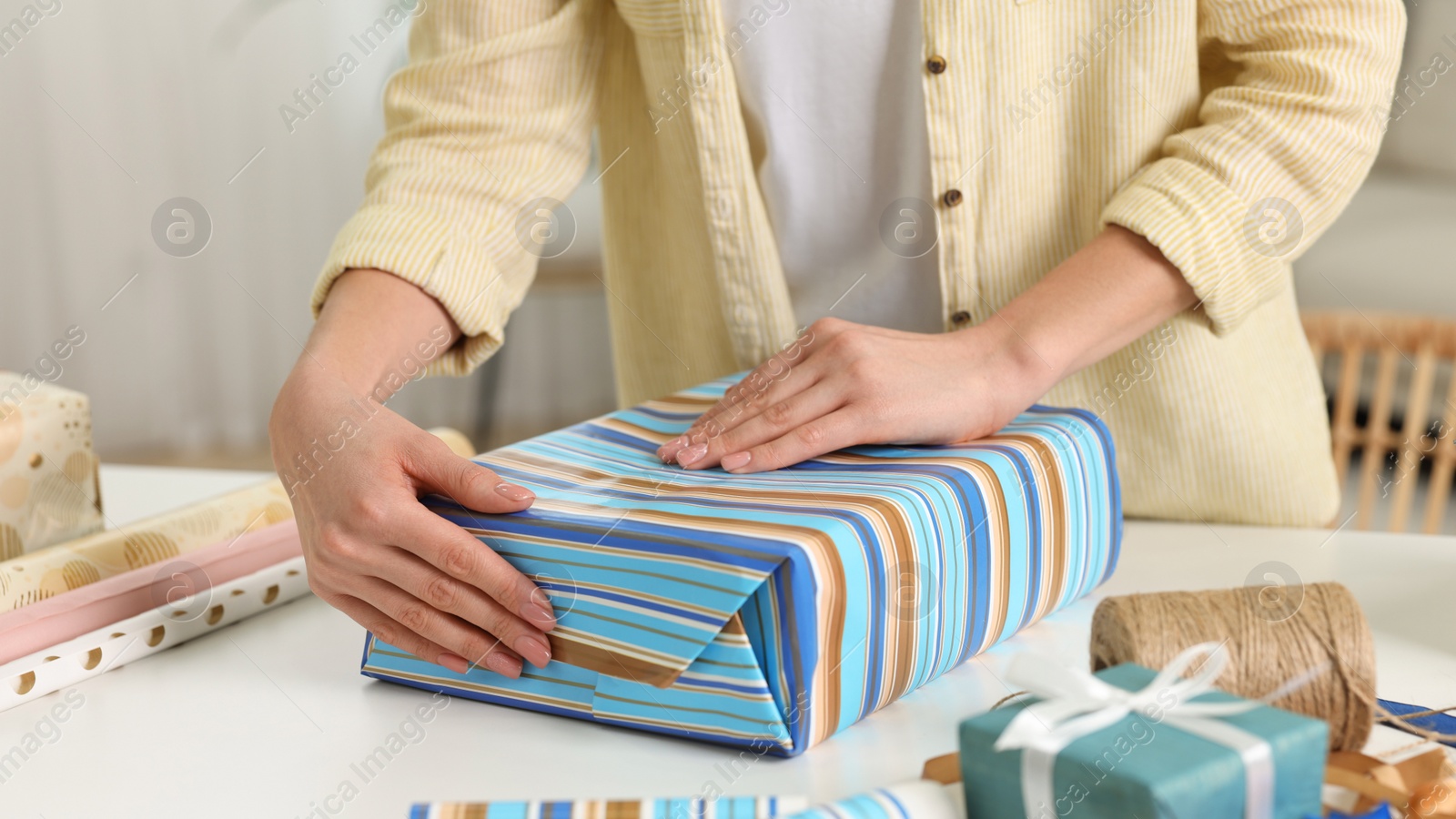 Photo of Woman wrapping gift at white table indoors, closeup