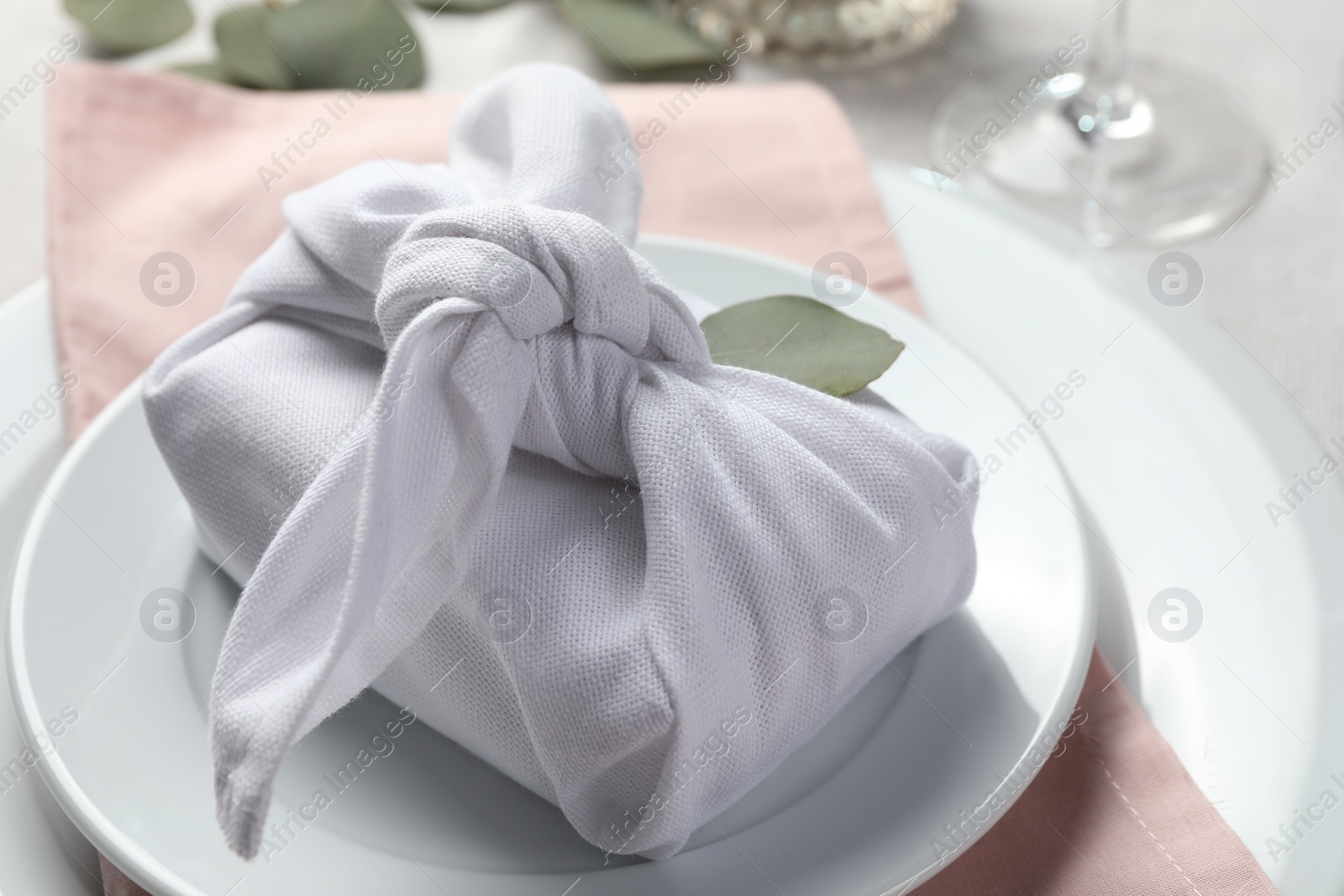 Photo of Furoshiki technique. Gift packed in white fabric and eucalyptus leaf on table, closeup