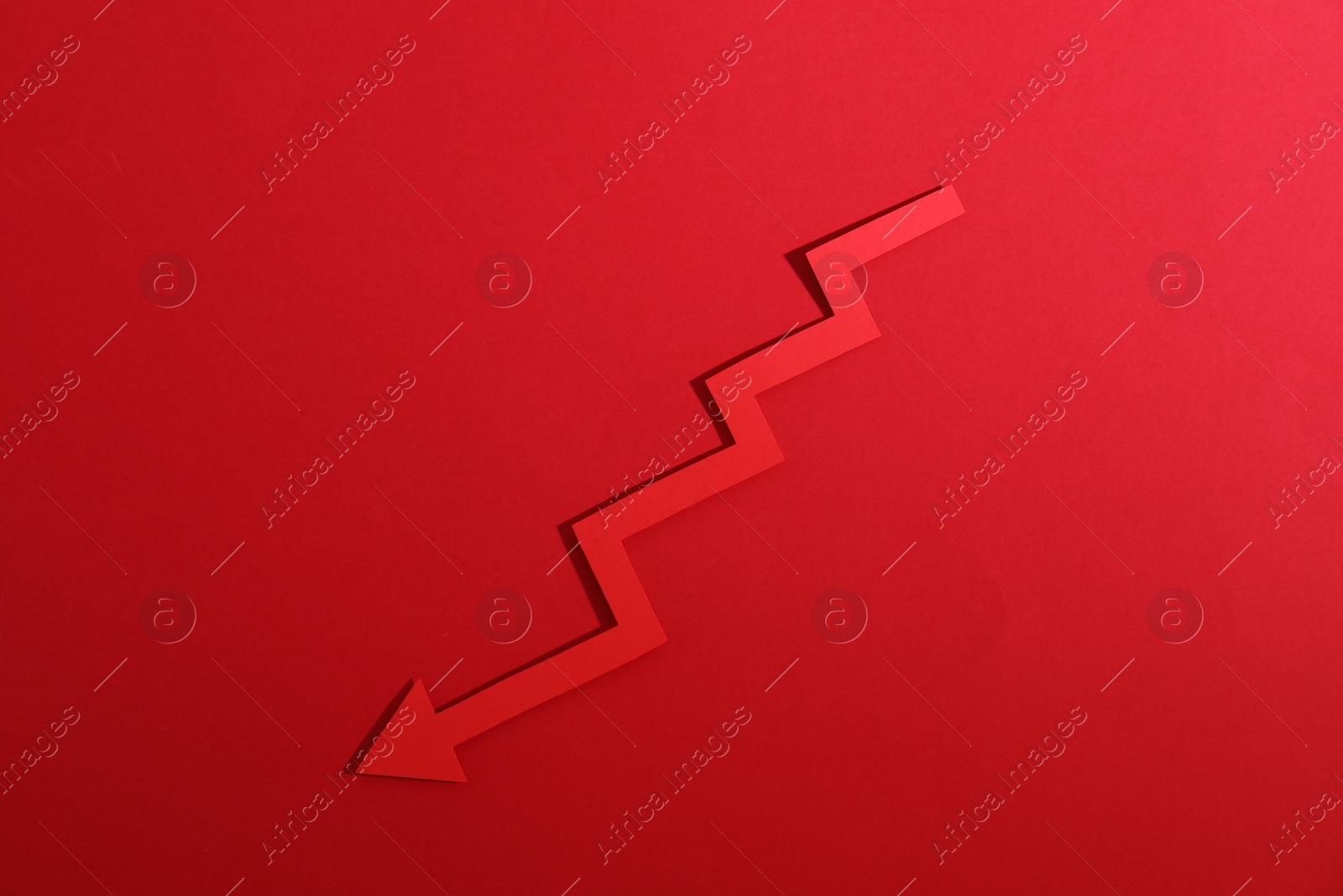 Photo of One zigzag paper arrow on red background, top view