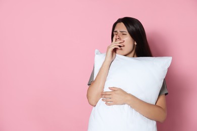 Photo of Sleepy young woman with soft pillow yawning on pink background, space for text