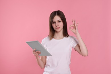 Photo of Portrait of happy teenage girl with tablet showing ok gesture on pink background