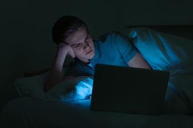 Photo of Teenage boy using laptop on bed at night. Internet addiction
