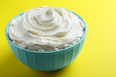 Photo of Bowl of tasty cream cheese on yellow background, closeup