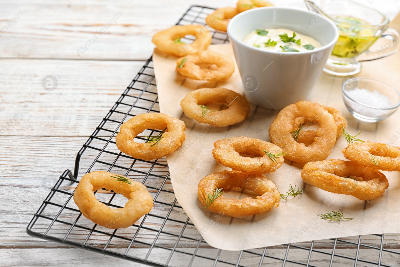 Photo of Cooling rack with fried onion rings and sauce on wooden background