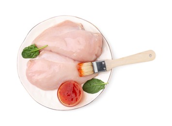 Marinade, basting brush and raw chicken fillets isolated on white, top view