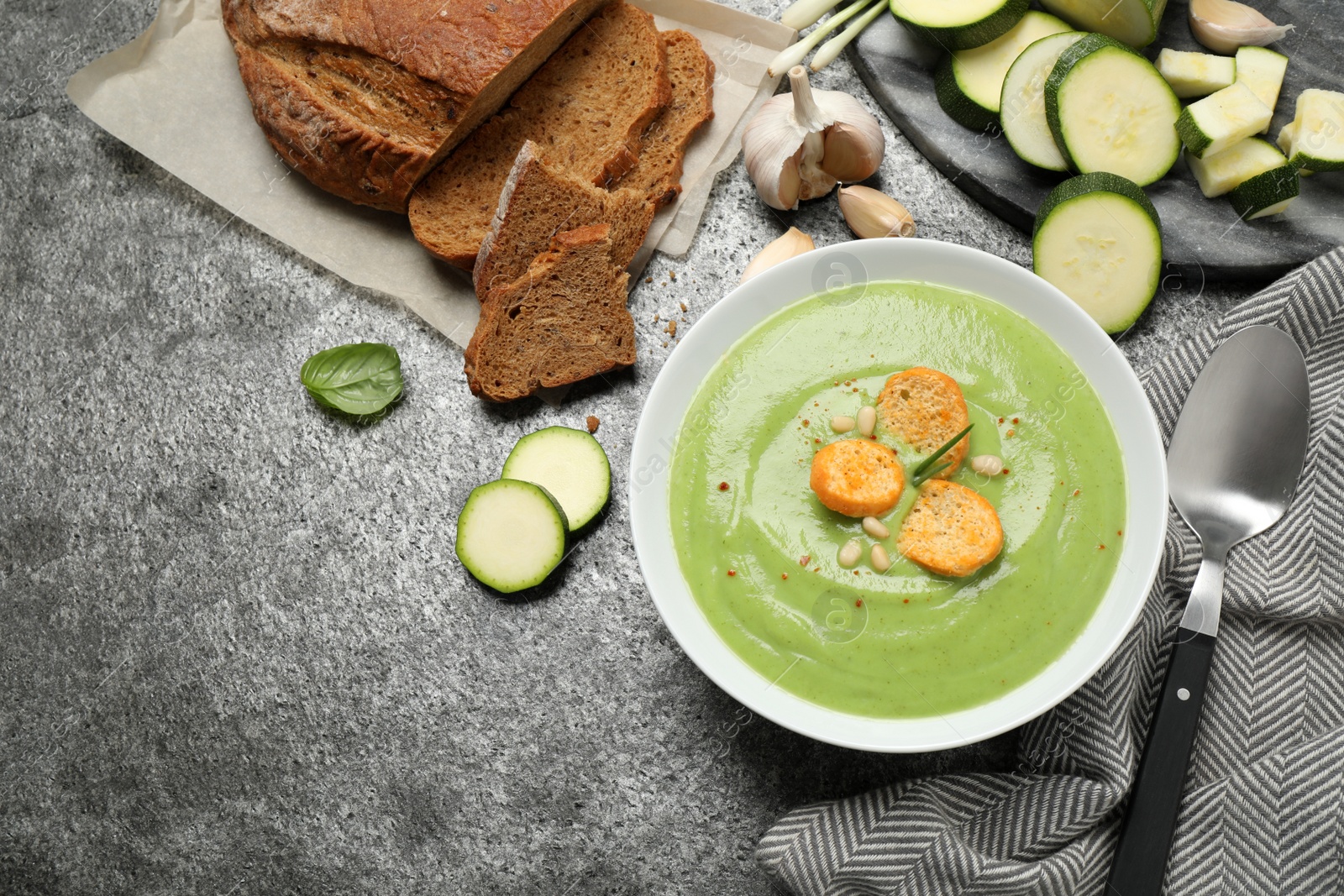 Photo of Tasty homemade zucchini cream soup served on grey table, flat lay
