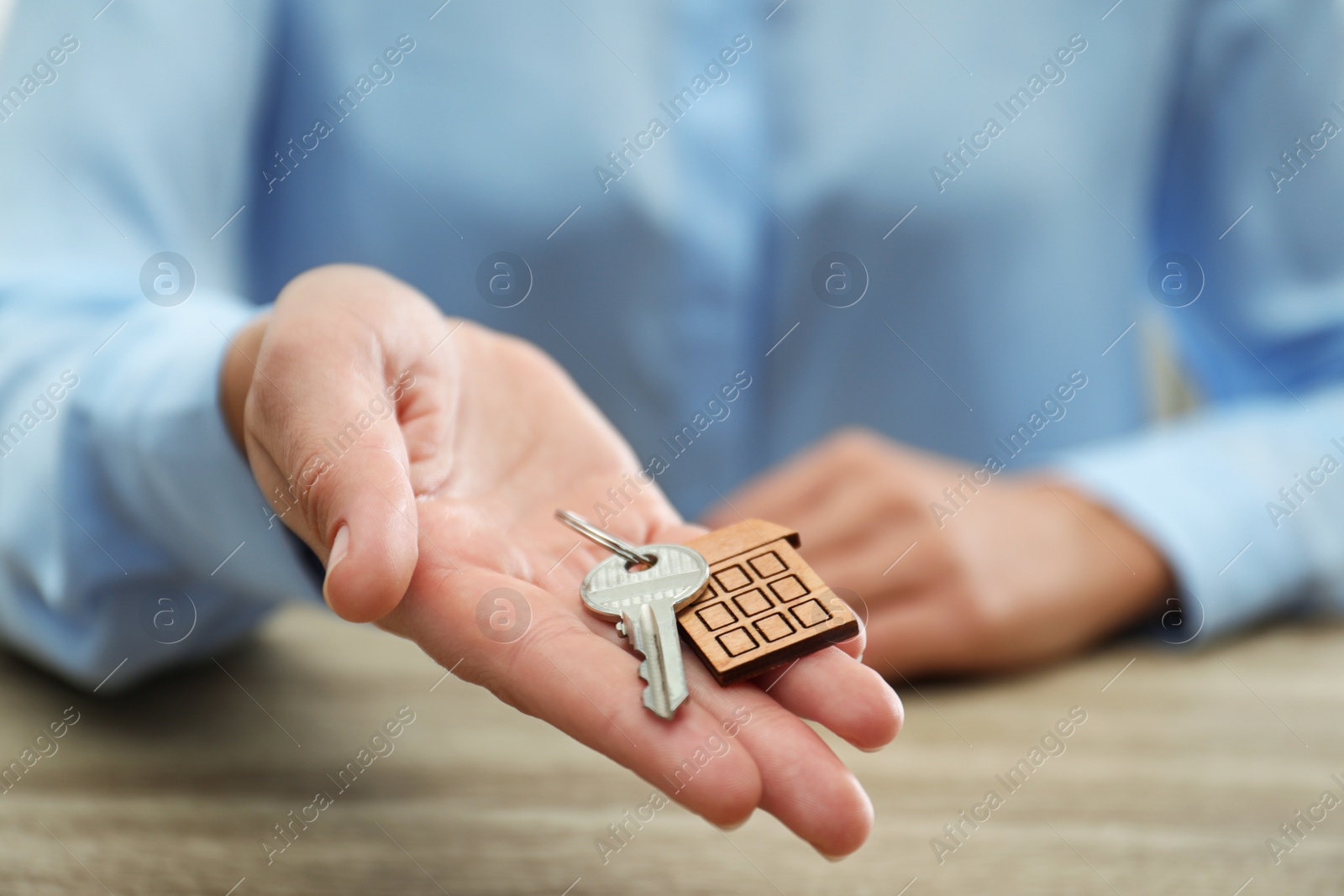 Photo of Real estate agent holding house key with trinket at wooden table, closeup