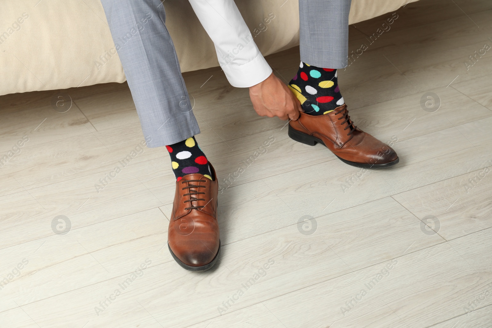 Photo of Man with colorful socks putting on stylish shoes indoors, closeup