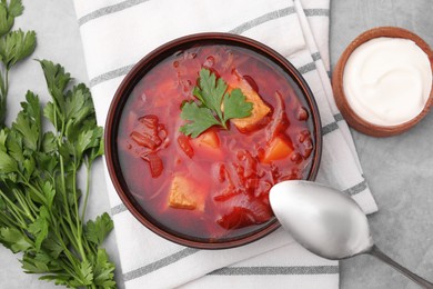 Photo of Bowl of delicious borscht, parsley and sour cream on light grey table, flat lay