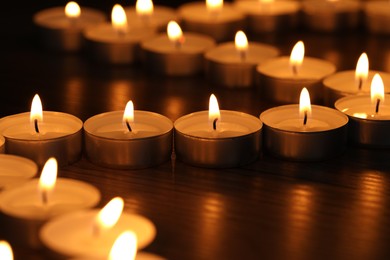 Photo of Burning tealight candles on dark surface, closeup