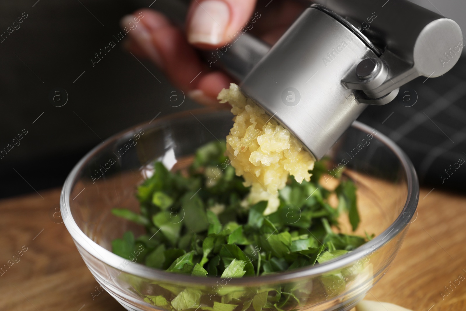 Photo of Woman squeezing garlic with press at wooden table, closeup