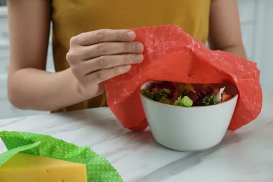 Photo of Woman covering tasty salad with beeswax food wrap at white marble table, closeup