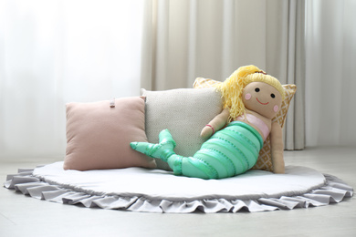 Photo of Funny toy mermaid near pillows on floor. Decor for children's room interior