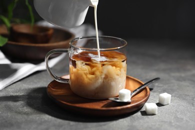 Photo of Pouring milk into cup of tea on grey table, closeup