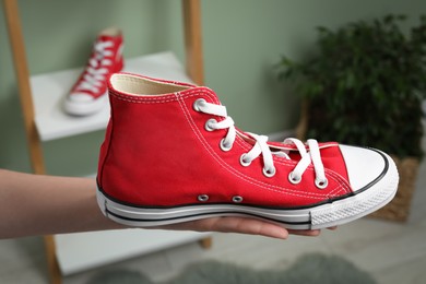 Woman holding new stylish red sneaker indoors, closeup