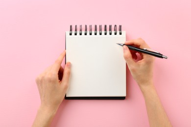 Photo of Woman writing in notebook on pink background, top view