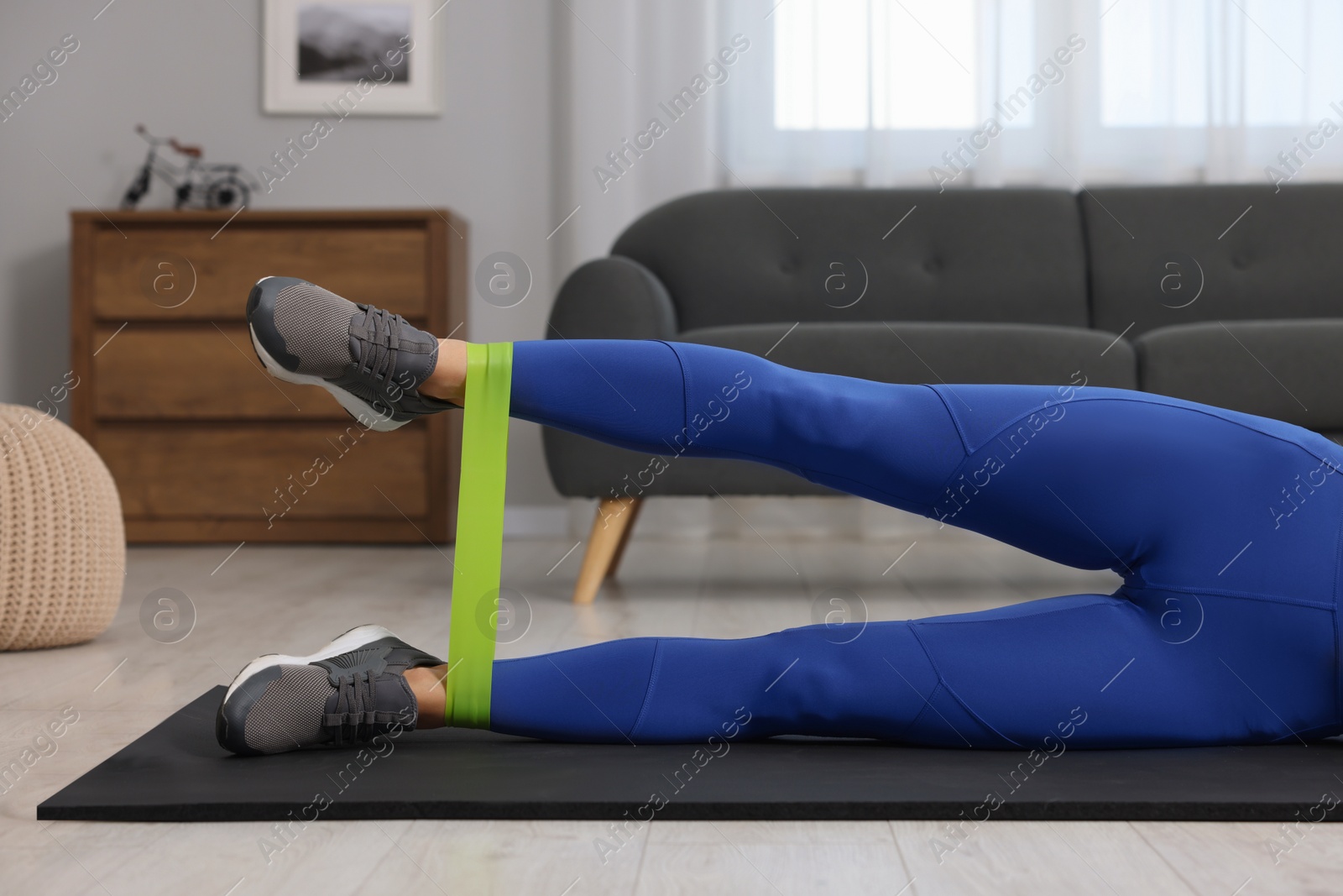 Photo of Woman doing exercise with fitness elastic band on mat at home, closeup