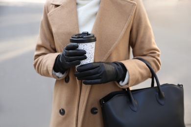 Photo of Woman with stylish leather gloves and cup of coffee outdoors, closeup