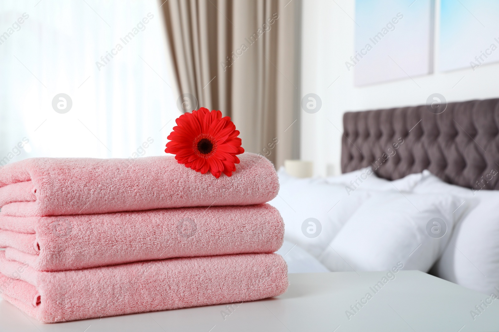 Photo of Stack of fresh towels with flower on table in bedroom. Space for text