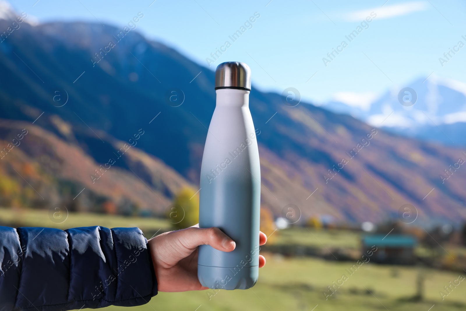 Photo of Boy holding thermo bottle with drink in mountains on sunny day, closeup