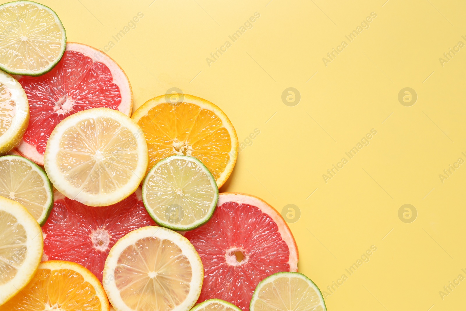 Photo of Different sliced citrus fruits on yellow table, top view. Space for text