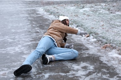 Photo of Young woman fallen on slippery icy pavement outdoors