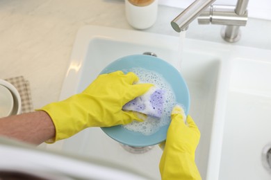 Man washing plate in kitchen sink, above view