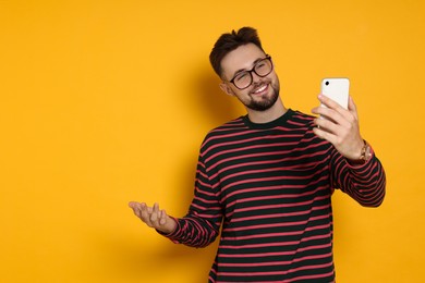 Photo of Handsome man in striped sweatshirt and eyeglasses with phone on yellow background, space for text