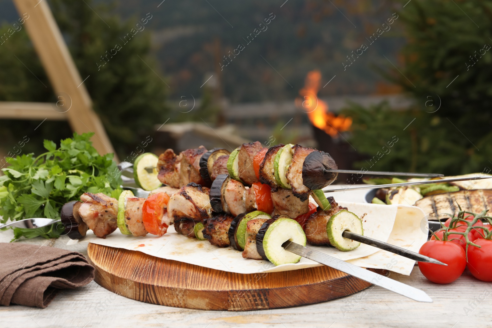 Photo of Metal skewers with delicious meat and vegetables served on wooden table outdoors