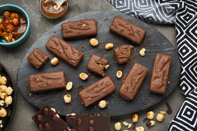 Delicious chocolate candy bars with caramel and nuts on grey table, flat lay