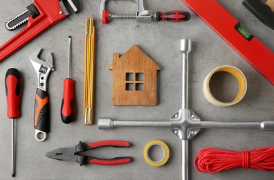 Photo of Flat lay composition with house figure and repair tools on grey stone table