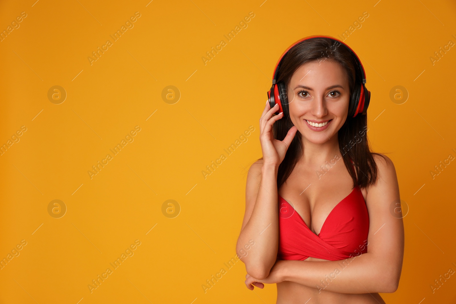 Photo of Pretty sexy woman with slim body in stylish red bikini and headphones on orange background, space for text
