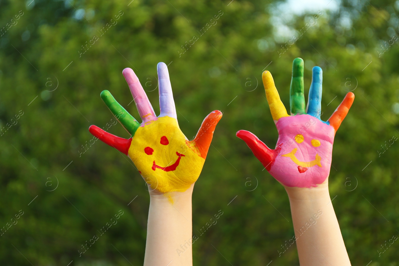 Photo of Kid with smiling face drawn on palms in green park, closeup. School holidays