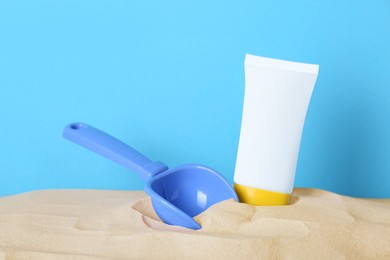 Photo of Suntan product and plastic beach toy in sand against light blue background