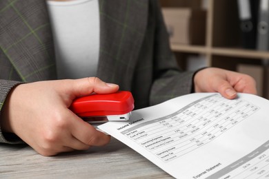 Photo of Woman stapling documents at wooden table indoors, closeup