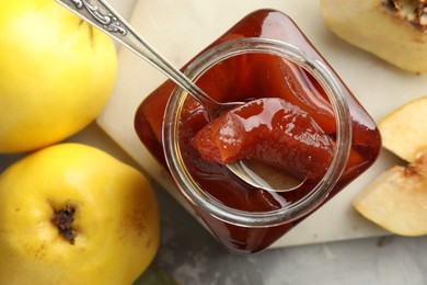 Photo of Taking tasty homemade quince jam from jar at table, flat lay