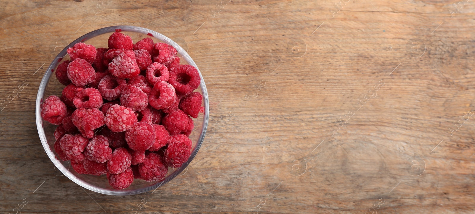 Photo of Tasty frozen raspberries on wooden table, top view. Space for text