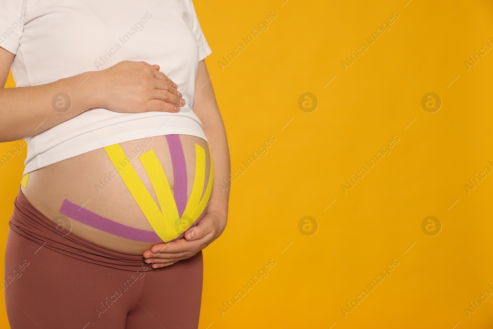 Photo of Pregnant woman with kinesio tapes on her belly against orange background, closeup. Space for text